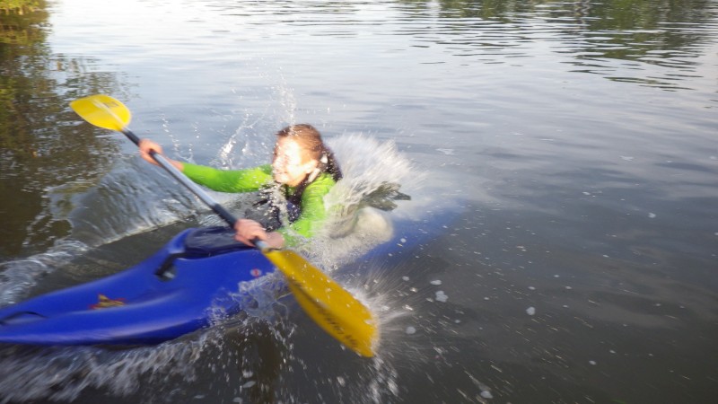 Paddlerin rutscht im Boot rückwärt eine Bootsrutsche runter und taucht ins Wasser ein.